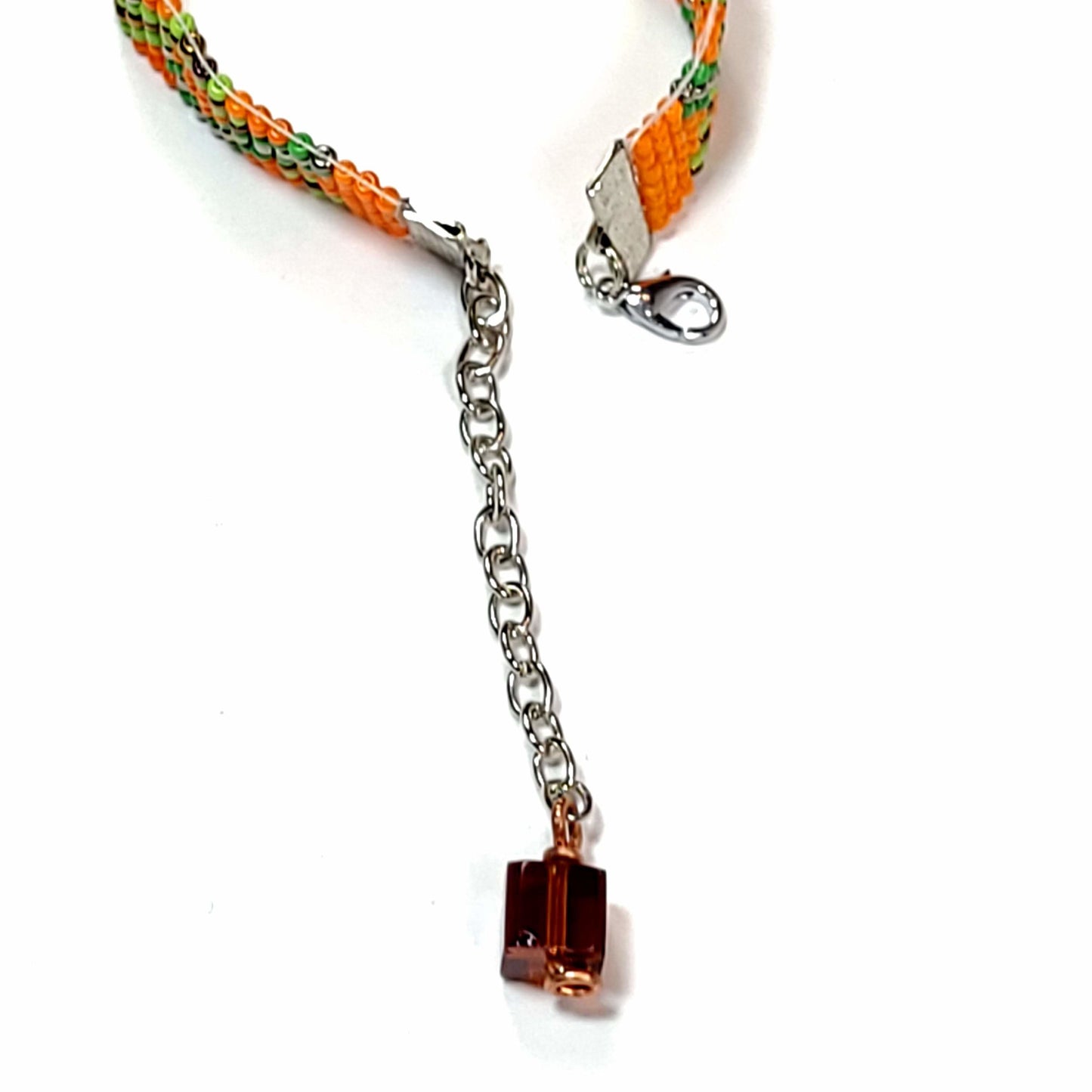 Clasp view of woven seed bead bracelet with orange, green, and black beads. Has a cute bead with copper wire accent on the extender.