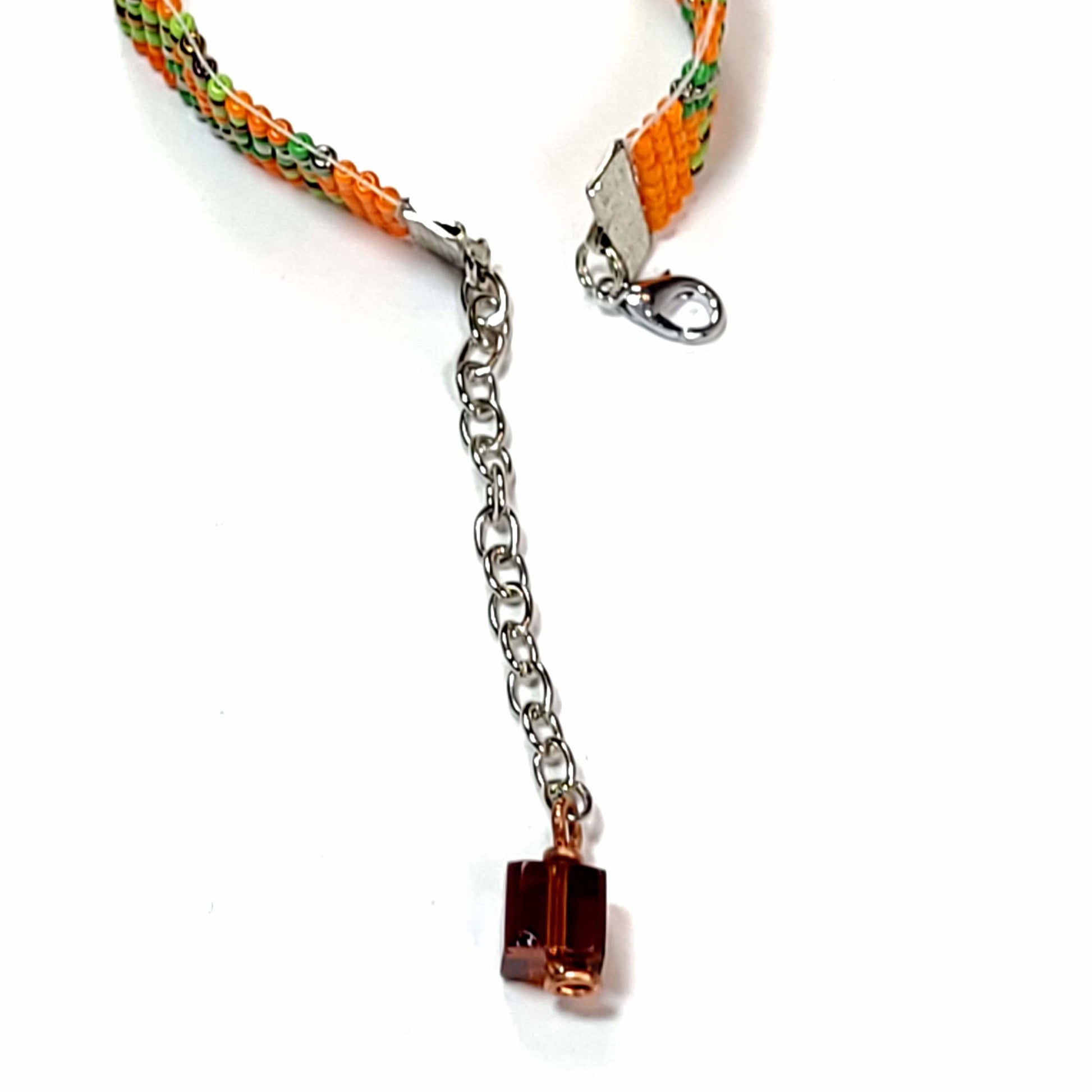 Clasp view of woven seed bead bracelet with orange, green, and black beads. Has a cute bead with copper wire accent on the extender.