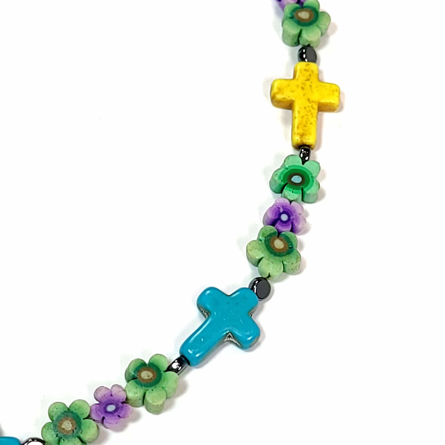 Close up of a polymer clay bead necklace with 6 blue cross, a 3 yellow crosses, and green and purple floral beads.