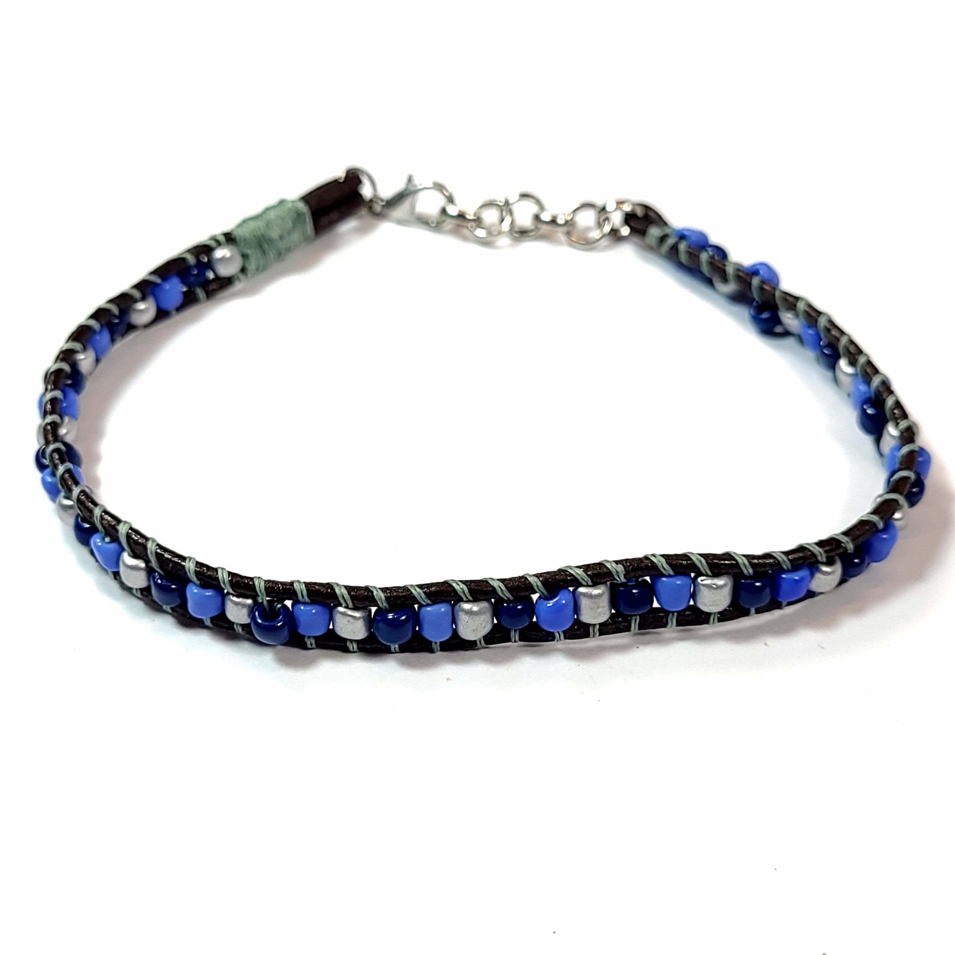 Light blue, dark blue, and gray beads flanked by brown leather, with greenish gray beading line bracelet.