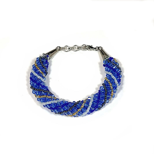 Bracelet made in a spiral pattern of blue bicone beads with gold tone, black, and white seed beads with silver one clasp.