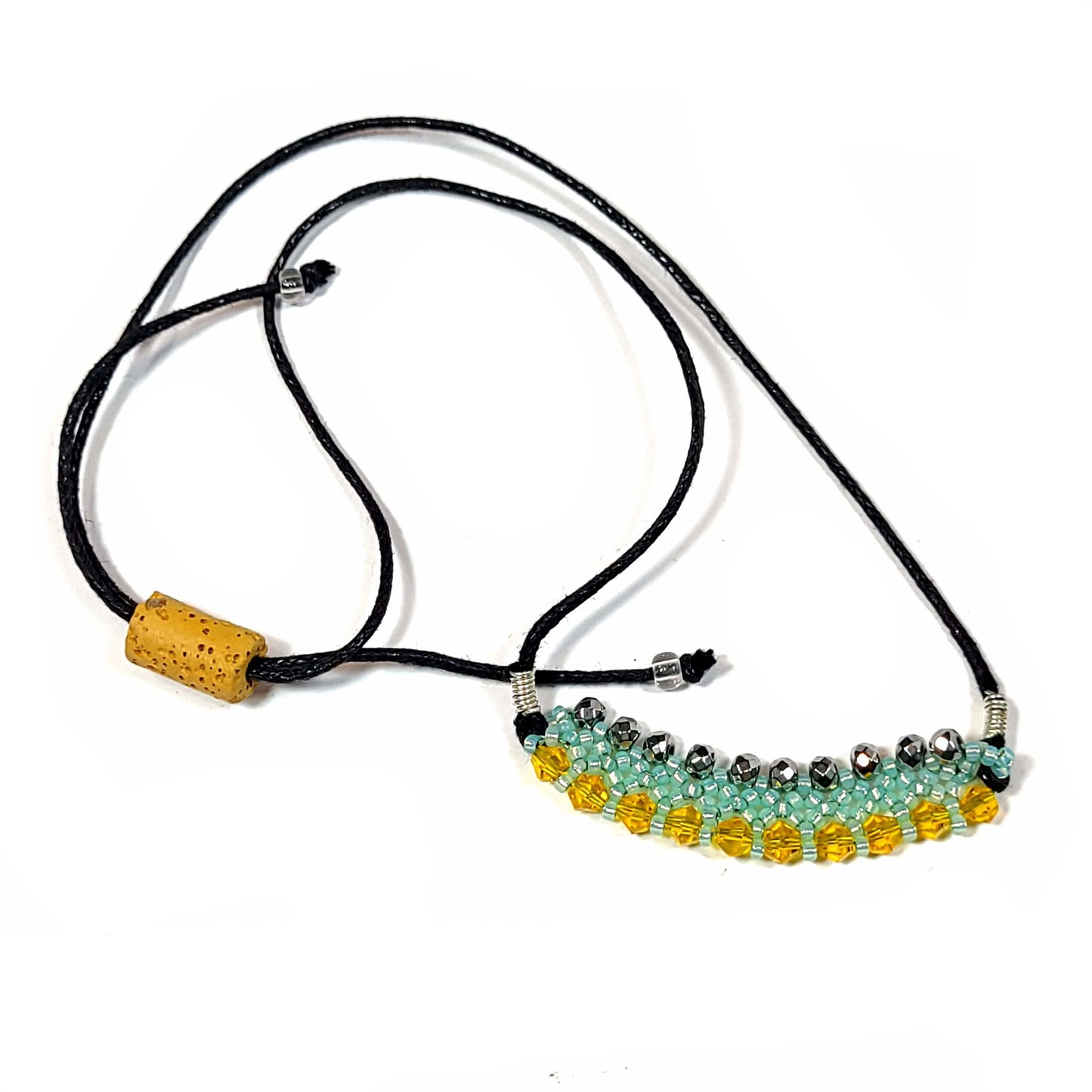 Necklace made with black silky cord that has a lava rock tube bead for adjusting the length. It has a pendant of aqua seed beads, yellow bicone, and hematite beads woven into a pendant.