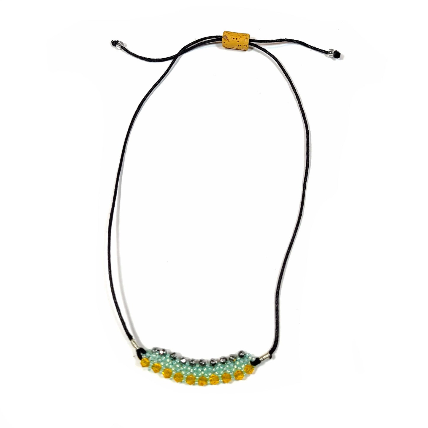 Necklace made with black silky cord that has a lava rock tube bead for adjusting the length. It has a pendant of aqua seed beads, yellow bicone, and hematite beads woven into a pendant.