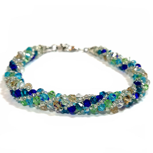 Bracelet made of teal, navy, light green, light blue, sand and crystal bicone beads with silver tone seed beads. It also has silver tone end caps, lobster clasp and extender chain. 